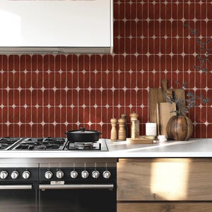 May include: A kitchen interior with a black cooker and oven, and a white worktop. The red and white oval-patterned tiles form the backsplash. Wooden chopping boards, a vase, and spice grinders are on the counter.