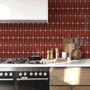 Op de afbeelding: Keukeninterieur met een zwart fornuis en oven en een wit aanrechtblad. De achterwand bestaat uit rood-witte tegels met een ovaal patroon. Houten snijplanken, een vaas en kruidenmolens staan op het aanrecht.
