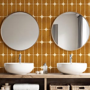 May include: A bathroom vanity featuring two circular mirrors, white washbasins, and chrome taps. The wooden vanity unit has a shelf with towels, candles, and baskets. The background showcases a retro tile pattern in brown and cream tones.