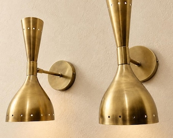 May include: Two wall sconces made of brushed brass metal. Each fixture features a dual-cone shape with a wide bottom shade and a narrower top section, both accented with a series of small circular perforations along the edges.