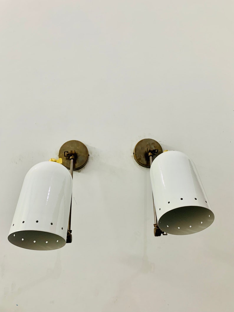 May include: A pair of white wall sconces with brass accents and a perforated design. The sconces are mounted on a white wall.