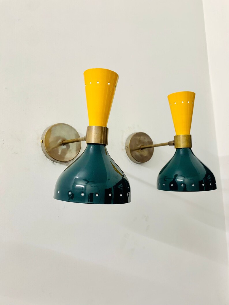 May include: Two wall sconces featuring a dual-tone design with a bright yellow conical top section and a dark green bell-shaped base. Each lamp has a metallic brass-toned wall mount, a horizontal arm, and small perforated holes along the edges.