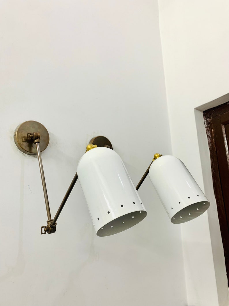 May include: Two white wall-mounted lights with brass accents and adjustable arms. The lights have a cylindrical shape with a perforated design.