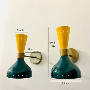 May include: Two wall sconces featuring a dark green dome-shaped base and a yellow conical top, connected by a brass-toned cylindrical centre. The lamps have small perforated holes along the edges. Dimensions shown are 3 inches, 8 inches, 10.5 inches, and 5 inches.