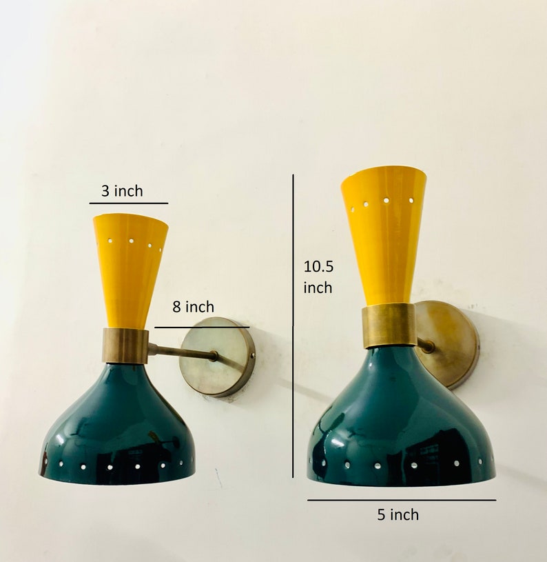 May include: Two wall sconces featuring a dark green dome-shaped base and a yellow conical top, connected by a brass-toned cylindrical centre. The lamps have small perforated holes along the edges. Dimensions shown are 3 inches, 8 inches, 10.5 inches, and 5 inches.