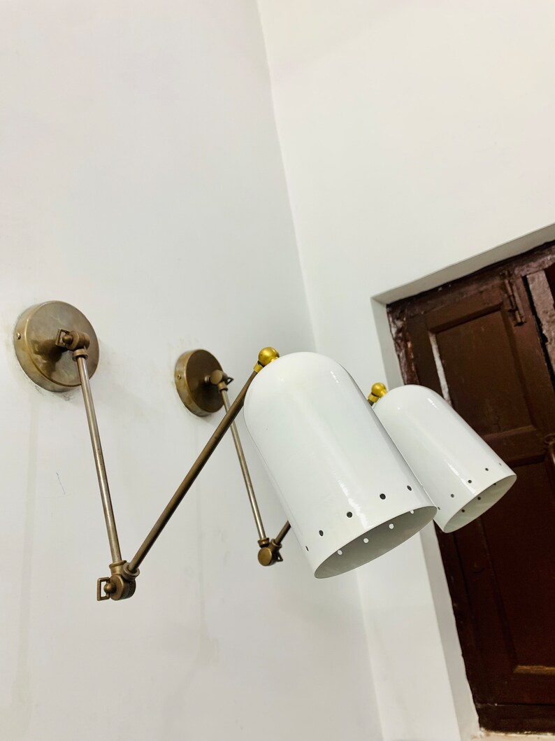 May include: A pair of white metal wall sconces with brass accents and adjustable arms. The sconces have a cylindrical shade with a row of small holes around the bottom.