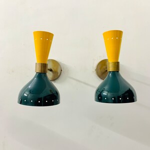 May include: A pair of wall sconces featuring a dual-tone design with a dark green, bell-shaped lower shade and a bright yellow, conical upper section. Both parts are accented with small, evenly spaced perforations and brass hardware.