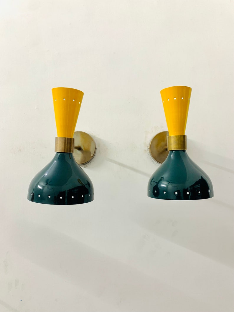 May include: A pair of wall sconces featuring a dual-tone design with a dark green, bell-shaped lower shade and a bright yellow, conical upper section. Both parts are accented with small, evenly spaced perforations and brass hardware.