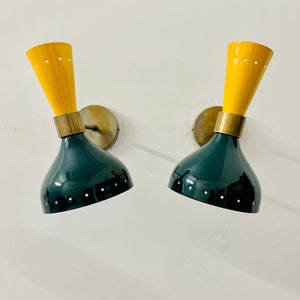 May include: A pair of wall sconces featuring a dual-tone design with a dark green, bell-shaped lower shade and a bright yellow, conical upper section. Each lamp includes a brass-coloured metal connector and a circular wall mounting plate.
