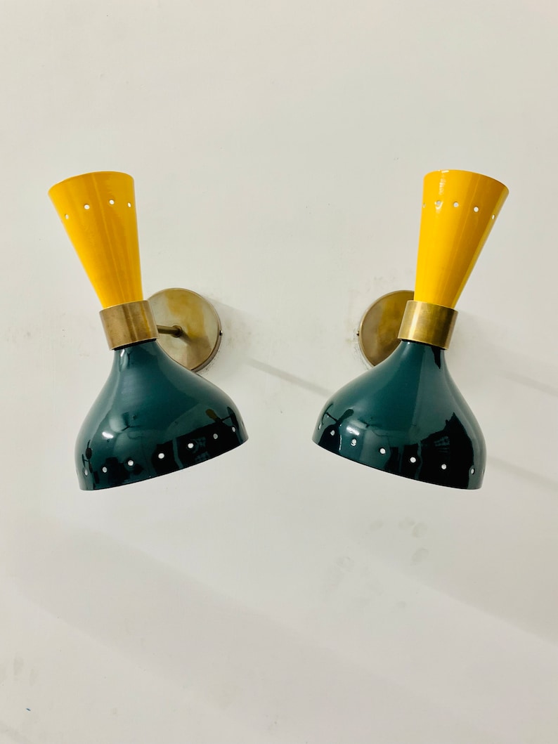 May include: A pair of wall sconces featuring a dual-tone design with a dark green, bell-shaped lower shade and a bright yellow, conical upper section. Each lamp includes a brass-coloured metal connector and a circular wall mounting plate.