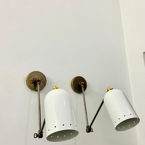 May include: Two white wall-mounted sconces with brass arms and a gold accent on the top of each shade. The shades have a pattern of small holes.