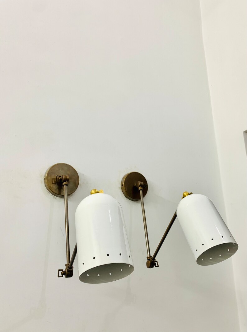 May include: Two white wall-mounted sconces with brass arms and a gold accent on the top of each shade. The shades have a pattern of small holes.