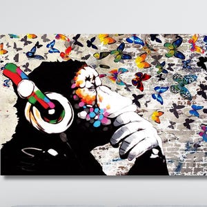 Peut inclure: Impression sur toile vibrante représentant une silhouette noire avec un casque, des papillons colorés s'échappant de la bouche. Le fond est un mur de briques texturé avec des éclaboussures de peinture.