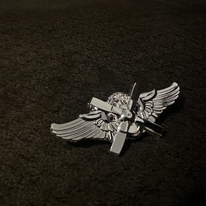 以下が含まれることがあります： プロペラと翼が付いた銀色のパイロットの翼バッジ。翼は広げられ、プロペラは中央にあります。