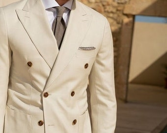 May include: A double-breasted suit in a light cream color with brown buttons. The suit has a pocket square in the left breast pocket and a gray tie.