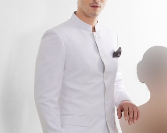May include: A white suit with a mandarin collar and button closure. The suit has a single pocket on the left side of the jacket. The man is wearing black shoes.
