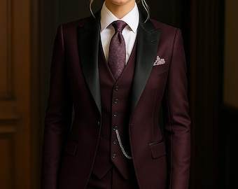 May include: A formal burgundy suit with a black satin lapel, white dress shirt, and burgundy tie. The three-piece suit includes a vest and matching trousers. A pocket square and watch chain add detail to the tailored ensemble.