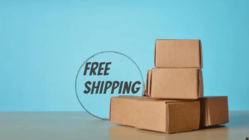 May include: A stack of four brown cardboard boxes on a light-colored surface against a blue background. A circular graphic with the words "FREE SHIPPING" is to the left of the boxes.