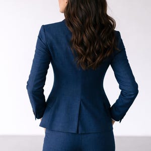 May include: A navy blue business suit, featuring a tailored blazer and matching trousers. The blazer has a classic two-button closure and a notched lapel. The suit is made of a textured fabric, and the person is facing away from the camera.