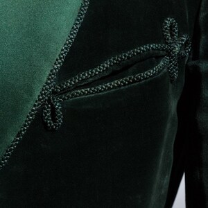 Pu&ograve; includere: Una giacca di velluto verde scuro con un bordo decorativo in corda nera. La giacca ha un dettaglio di tasca unico con un bordo in corda.