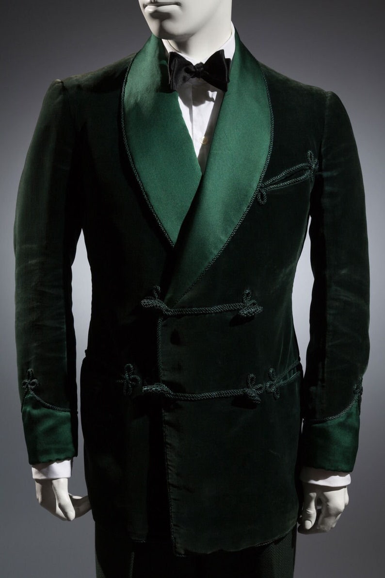 Pu&ograve; includere: Una giacca di velluto verde scuro con un colletto a scialle di raso e dettagli decorativi in corda. La giacca ha una chiusura a doppio petto e maniche lunghe.