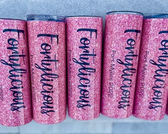 Puede incluir: Seis vasos de plástico rosa con purpurina con letras negras que dicen "Fortylicious" y "Fort Myers 2022".
