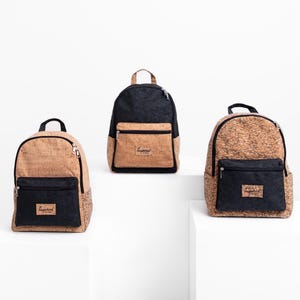 May include: Three backpacks with a cork-like texture and black accents. Each bag has a front pocket and a top handle. The bags are displayed on white platforms against a white background. The front pocket of each bag has the word "Inspired" on it.