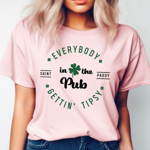 Puede incluir: Camiseta rosa con un tr&eacute;bol verde y el texto "Everybody in the Pub Gettin' Tipsy" en un c&iacute;rculo a su alrededor. El texto "Saint Paddy" est&aacute; en la parte superior del c&iacute;rculo.