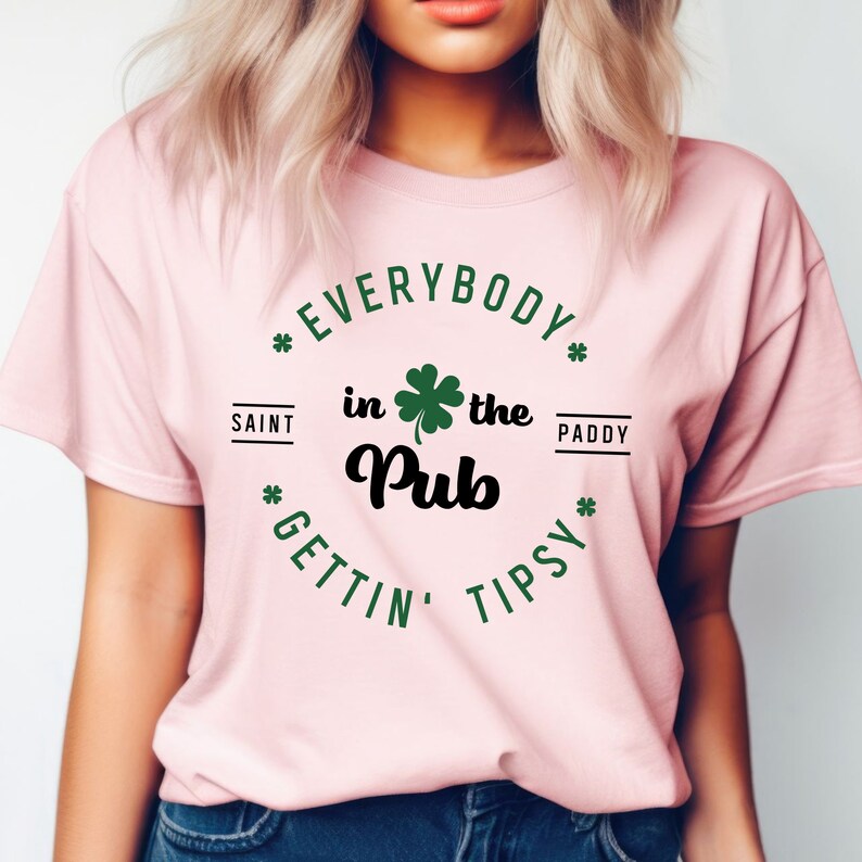 Puede incluir: Camiseta rosa con un tr&eacute;bol verde y el texto "Everybody in the Pub Gettin' Tipsy" en un c&iacute;rculo a su alrededor. El texto "Saint Paddy" est&aacute; en la parte superior del c&iacute;rculo.
