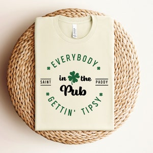 Puede incluir: Una camiseta verde claro con un gr&aacute;fico negro y verde que dice "Everybody in the Pub Gettin' Tipsy" con un dise&ntilde;o de tr&eacute;bol.