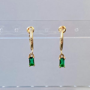 Puede incluir: Pendientes de aro dorados con una piedra rectangular verde esmeralda colgante.