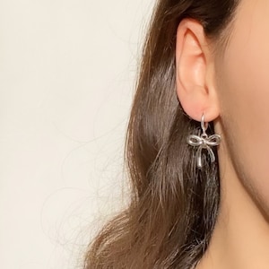以下が含まれることがあります： シルバーの弓形ドロップイヤリング。イヤリングは小さく繊細で、シンプルなデザインです。
