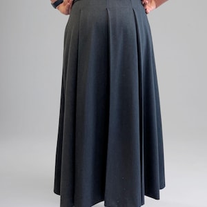 May include: A dark gray maxi skirt with a pleated front and a fitted waistband. The skirt is made of a smooth, woven fabric.