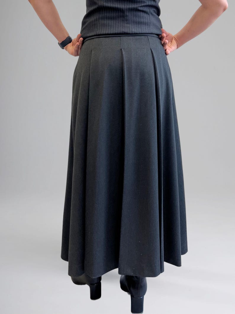 May include: A dark gray maxi skirt with a pleated front and a fitted waistband. The skirt is made of a smooth, woven fabric.