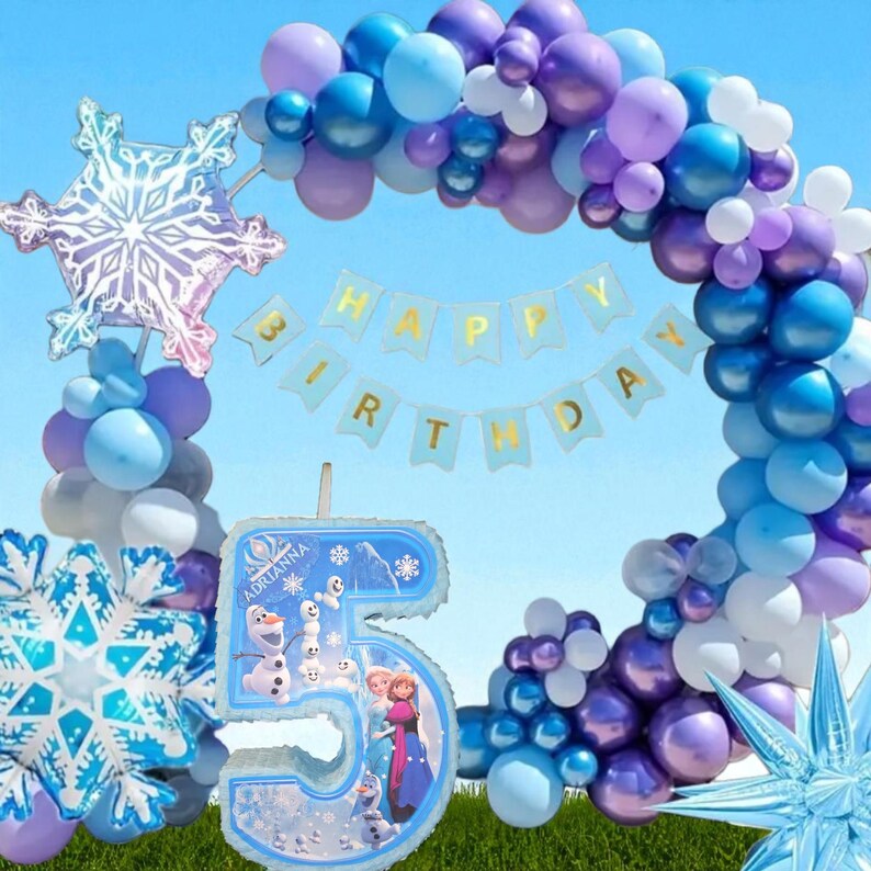 Puede incluir: Una escena festiva de cumplea&ntilde;os con un arco de globos azules y morados, decoraciones de copos de nieve y una pancarta que dice "HAPPY BIRTHDAY". Un gran globo con el n&uacute;mero 5 presenta personajes de la pel&iacute;cula Frozen. El escenario es un cielo azul.