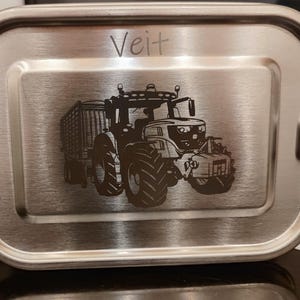 Könnte beinhalten: Eine Edelstahl-Lunchbox mit einem schwarz-weißen Bild eines Traktors und dem Namen "Veit" auf der Vorderseite.