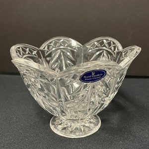 May include: A clear glass bowl with a scalloped rim and intricate cut designs. The bowl is on a pedestal base and has a blue label that reads "Royal Doulton Finest Crystal".