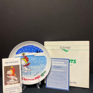 May include: A collector's plate featuring Snoopy ice skating, with the text "Merry Christmas 1982." Includes a certificate of authenticity and a box. The plate is a collectible from Schmid.