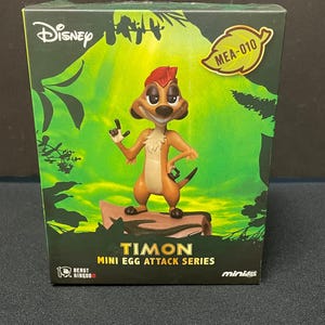 May include: A brown and tan Timon figurine from Disney's The Lion King. The figurine is part of the Beast Kingdom Mini Egg Attack Series. The box features a green jungle background with the text "Disney" and "Timon Mini Egg Attack Series".