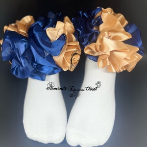 May include: A pair of white socks with navy blue and gold satin ribbon accents. The socks have a ruffled design at the top. The text "Armani's Elegant Closet" is printed on the socks.