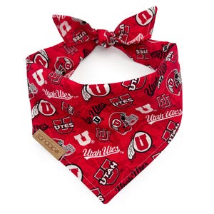 May include: Red and white dog bandana with a repeated pattern of the University of Utah logo, including the words "Utah Utes" and "UTES".