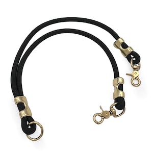 Op de afbeelding: Twee zwarte handvatten voor handtassen van touw met goudkleurige metalen hardware. Elk handvat heeft een lus aan één uiteinde en een sluiting aan het andere uiteinde, ontworpen voor eenvoudige bevestiging aan een tas. De handvatten zijn gebogen en liggen op een witte achtergrond.