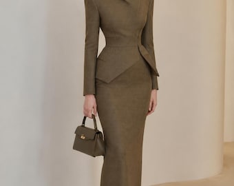 May include: An olive green long-sleeved jacket with a high collar and structured shoulders paired with a matching floor-length maxi skirt. The ensemble is accompanied by a small olive green structured handbag with a top handle and gold hardware.