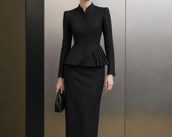 May include: A black two-piece suit consisting of a long-sleeved jacket with a mandarin collar and a pleated peplum waist, paired with a matching knee-length pencil skirt. The ensemble is completed with black pointed-toe heels and a small black clutch.