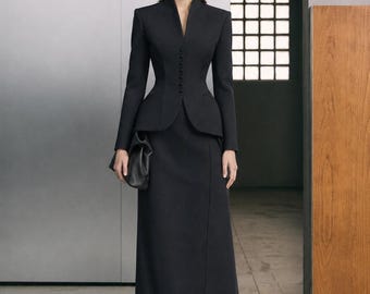 May include: A black long-sleeved jacket with a high collar and a row of small buttons, paired with a matching floor-length skirt featuring a front slit. The jacket has a peplum waist, and a black clutch is held in one hand.