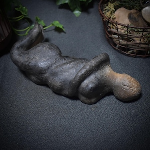 Könnte beinhalten: Eine dunkelgraue Keramikskulptur einer zusammengerollten Figur. Die Skulptur ist glatt und hat eine leicht strukturierte Oberfläche.