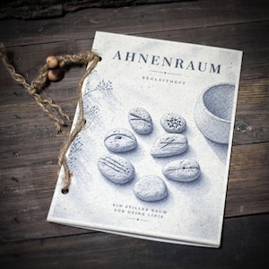 May include: A booklet titled AHNENRAUM BEGLEITHEFT with a light gray cover featuring illustrations of seven textured stones and a bowl. The booklet is bound with a piece of brown twine and two wooden beads attached to the top left corner.