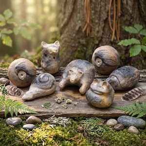 Könnte beinhalten: Eine Sammlung von sechs handgefertigten Tonfiguren in Form eines Bären, eines Frosches, einer Schildkröte, einer Schnecke und zwei kugelförmigen Wesen mit Vogelgravuren. Die Skulpturen haben eine natürliche Oberfläche in Grau- und Beigetönen.
