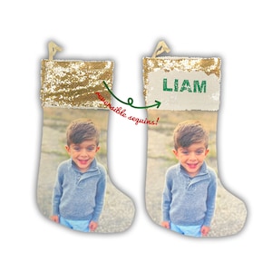 May include: Two Christmas stockings with reversible gold sequins at the top. One stocking displays the name "LIAM" in green letters. The stockings feature a photo of a smiling child. The text "reversible sequins!" is also present.
