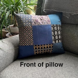 May include: A patchwork pillow with various patterned fabric squares in shades of blue, black, and purple. The pillow is resting on a gray upholstered chair. The text "Front of pillow" is visible.